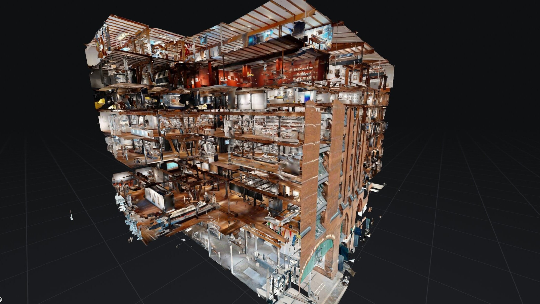Aufgeschnittenes 3D‑Dollhouse-Modell eines mehrgeschossigen Geb&auml;udes, das freigelegte Etagen, R&auml;ume, Treppen, M&ouml;bel und eine Backsteinfassade mit Bogenportal vor dunklem Rasterhintergrund zeigt.