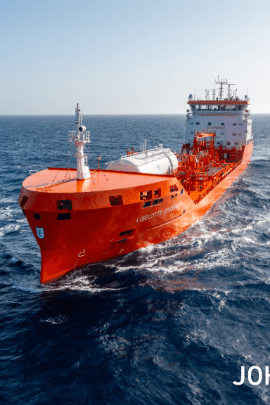 Roter Flüssiggastanker fährt quer über tiefblaues, leicht welliges Meer, Bug frontal, sichtbare Aufbauten und Decks, leichte Gischt, klarer Horizont.