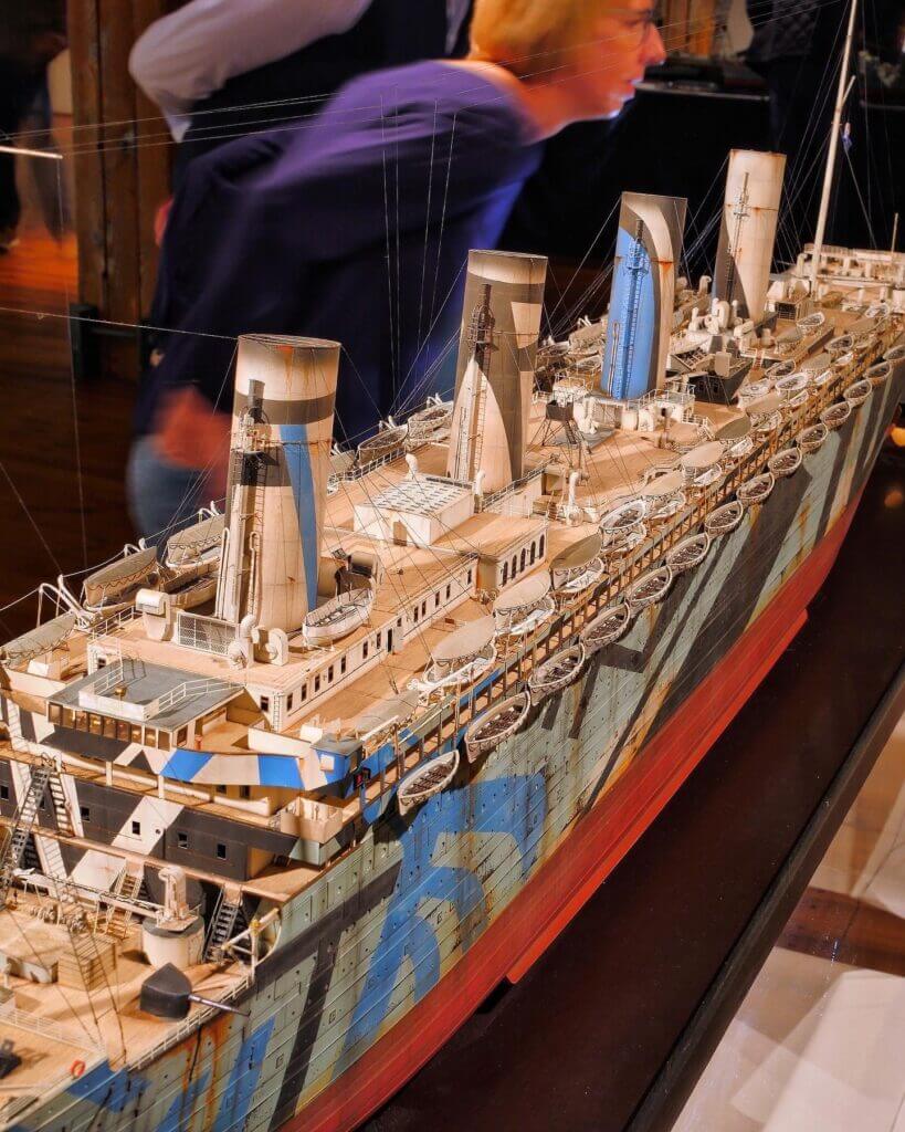 Detailliertes Schiffsmodell mit vier Schornsteinen, zahlreichen Rettungsbooten und auffälliger Dazzle‑Tarnung in Blau, Grau und Rot im Museum.