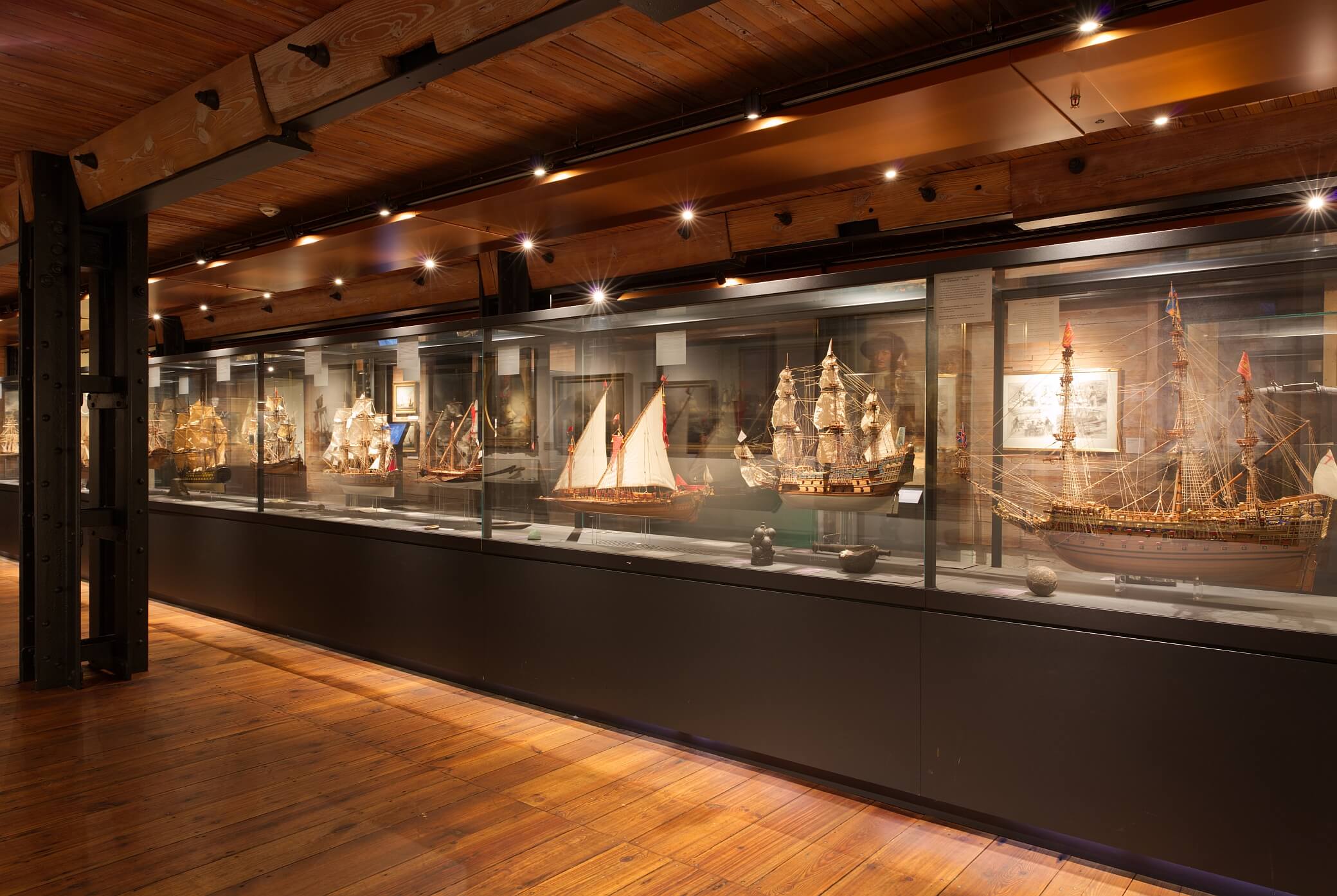 Glasvitrine mit mehreren historischen Schiffsmodellen in warm beleuchtetem Museumsraum mit Holzfußboden.