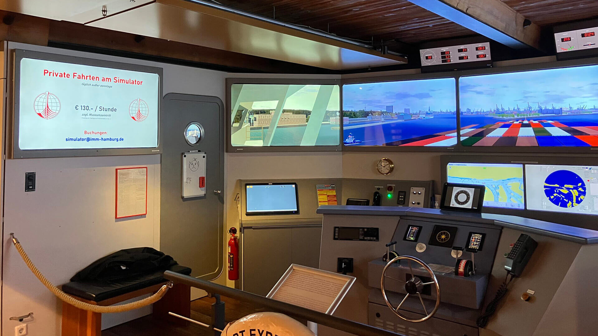 Schiffsbr&uuml;ckensimulator mit Panorama-Bildschirmen, Steuerrad und sichtbarer Preisanzeige f&uuml;r private Fahrten.
