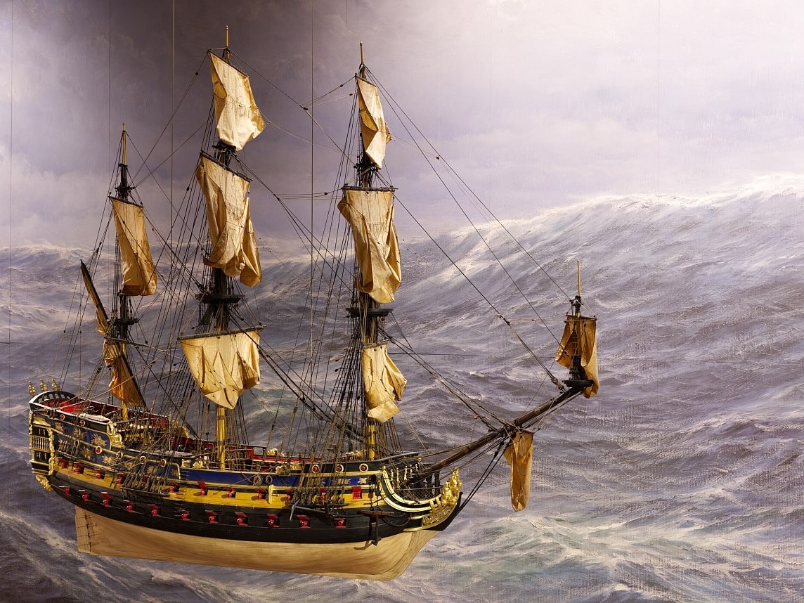 Detailliertes Modell eines dreimastigen Segelschiffs mit gebräunten Segeln und verziertem Rumpf vor aufgewühlter graublauer See.