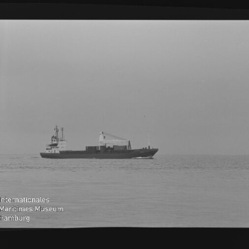 Kleines Frachtschiff in Seitenansicht auf ruhiger See in Schwarzweiß, unten links Wasserzeichen des Maritimen Museums Hamburg