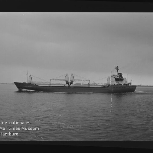 Frachtschiff mit Ladekränen und achternliegendem Aufbau fährt über ruhige See; Schwarzweißaufnahme mit Museumslogo