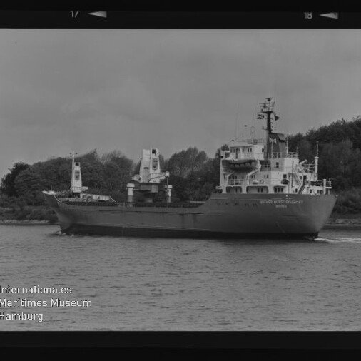 Schwarzweißfoto eines Frachtschiffs, das an einem bewaldeten Ufer vorbeifährt, unten links das Logo Maritimes Museum Hamburg.