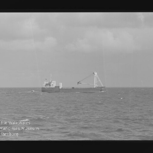 Frachtschiff mit Auslegerkran auf ruhiger See unter bewölktem Himmel, Filmrand und Wasserzeichen Maritimes Museum Hamburg.