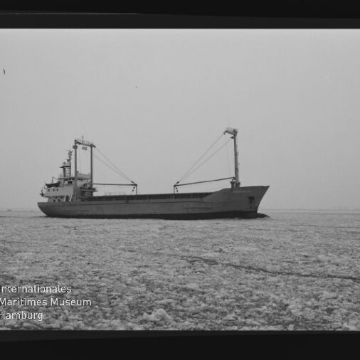Schwarzweiß-Foto eines Frachtschiffs mit zwei Ladekränen, das durch eine vereiste See fährt; Museumssignet unten links.