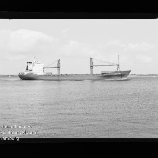 Frachtschiff mit zwei Ladekränen fährt auf ruhiger See, schwarz-weiße Aufnahme mit sichtbarem Filmrand.