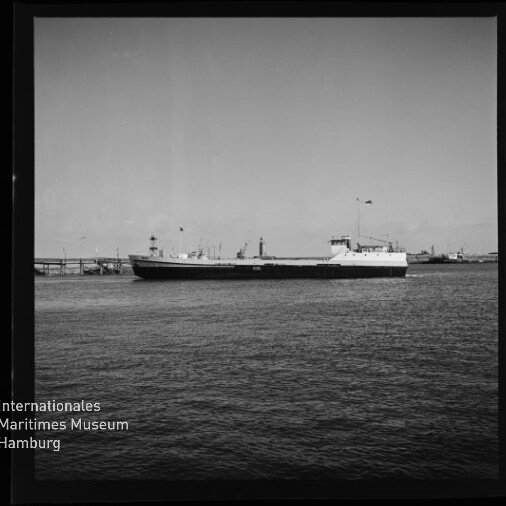 Großer Frachter am Kai auf ruhigem Wasser, schwarzweiß; Museumslogo Internationales Maritimes Museum Hamburg in der Ecke.