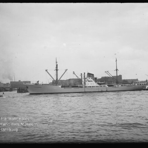 Frachtschiff im Hafen vor Kränen und Lagerhallen, Wasser im Vordergrund; Wasserzeichen: Int. Maritimes Museum Hamburg