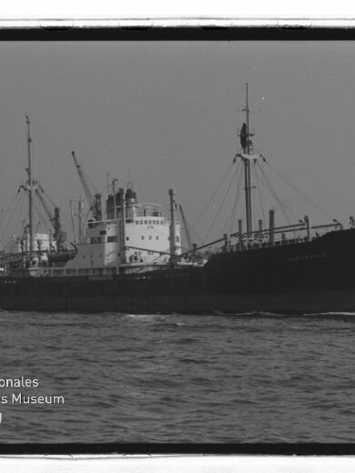 Frachtschiff mit mehreren Masten und rauchendem Schornstein im Hafen; Wasserzeichen Internationales Maritimes Museum Hamburg unten links.