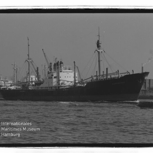 Frachtschiff mit mehreren Masten und rauchendem Schornstein im Hafen; Wasserzeichen Internationales Maritimes Museum Hamburg unten links.