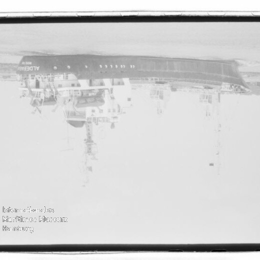 Schwarzweiß-Fotonegativ eines am Kai liegenden Passagierschiffs, kopfüber gezeigt, mit sichtbarem Filmrand und Museumswasserzeichen.