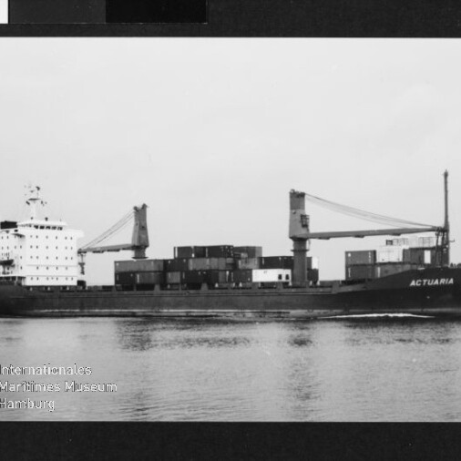 Frachtschiff ACTUARIA mit aufgestapelten Containern und zwei Ladekränen fährt auf ruhiger See, Museumslogo unten links.