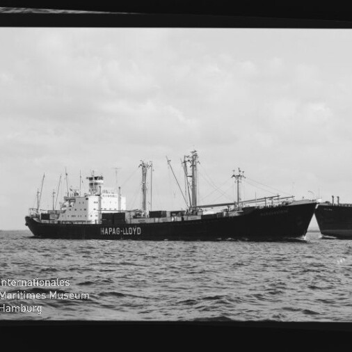 Frachtschiff mit HAPAG-LLOYD-Schriftzug, Ladekräne und Masten auf ruhiger See; Schwarzweißaufnahme mit Museumslogo.