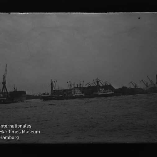 Hafen mit Kränen und Schiffen, Wasser im Vordergrund; Logo des Internationalen Maritimen Museums Hamburg links unten.