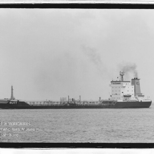 Schwarzweißfoto eines Tankschiffs mit Namen BUTT, rauchender Schornstein auf ruhiger See; Museumslogo unten links.