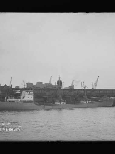 Großes Schiff am Industriehafen vor Lagerhallen und Kränen, Tonnenboje im Vordergrund; Schriftzug 