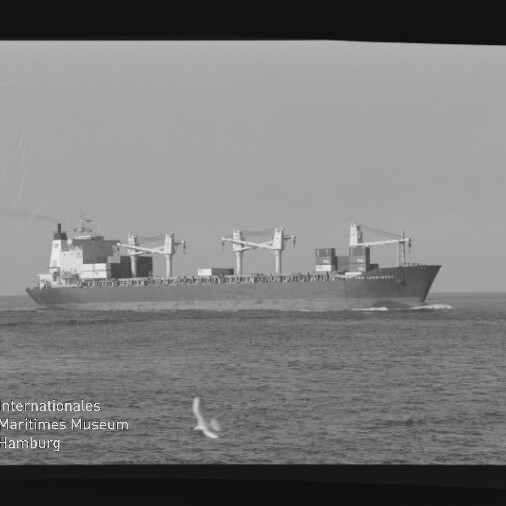 Schwarz-weiß-Foto eines Frachtschiffs mit Ladekränen und Containern auf ruhiger See, Möwe im Vordergrund und Museumsschriftzug