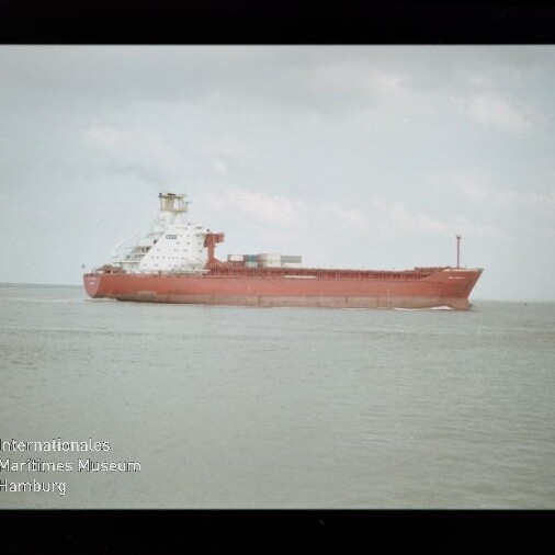 Rotes Frachtschiff auf ruhiger See, Filmränder sichtbar und Museum-Logo unten links.