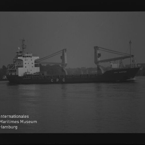 Frachtschiff mit zwei Ladekränen und 'CPC' am Rumpf auf ruhigem Wasser vor Hafenkulisse; Museumslogo links.