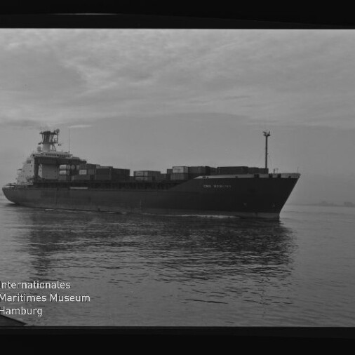 Schwarzweißaufnahme eines Containerschiffs mit gestapelten Frachtcontainern auf ruhiger See, Filmrahmen und Museumswasserzeichen.