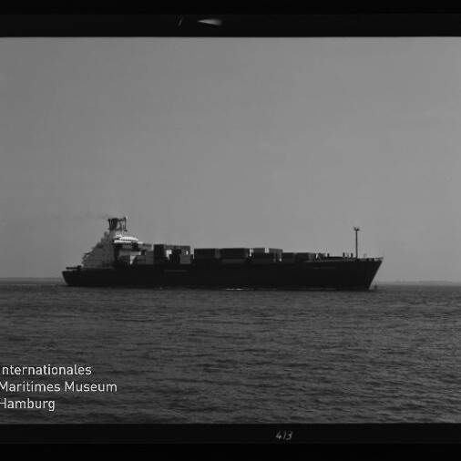 Schwarzweißaufnahme eines Containerschiffs auf ruhiger See, mit Containerstapel und Museumslogo unten links.