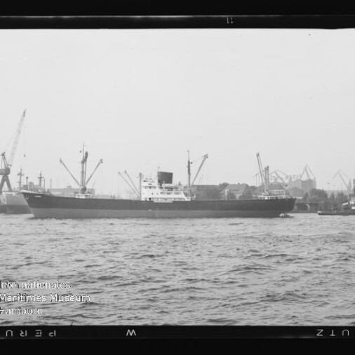 Frachtschiff im Hafen vor Kränen, begleitet von einem kleinen Schlepper, schwarzweißes Bild.