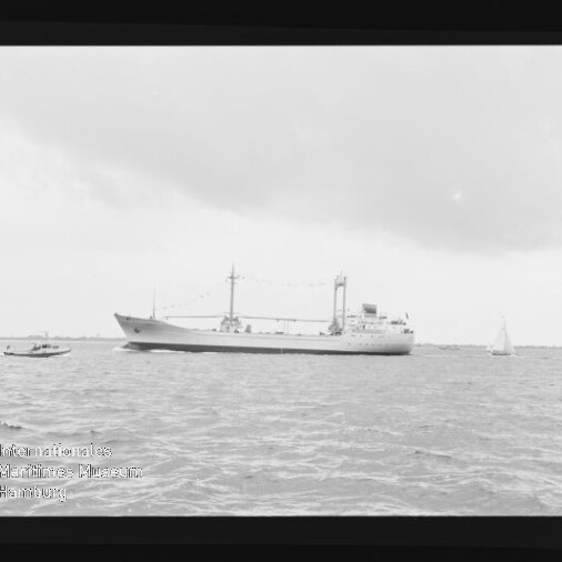 Großes Frachtschiff mit Deckaufbauten und Ladekränen auf ruhiger See, daneben ein Motorboot und ein Segelboot; Wasserzeichen Internationales Maritimes Museum Hamburg