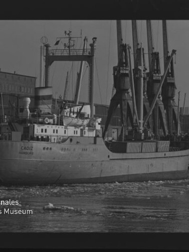 Frachtschiff CADIZ am Kai neben hohen Ladekranen, Eisstücke im Wasser und Museums-Wasserzeichen unten links.