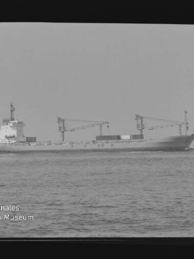 Frachtschiff mit zwei Ladekränen auf ruhiger See, schwarzweißes Foto mit Wasserzeichen Internationales Maritimes Museum Hamburg