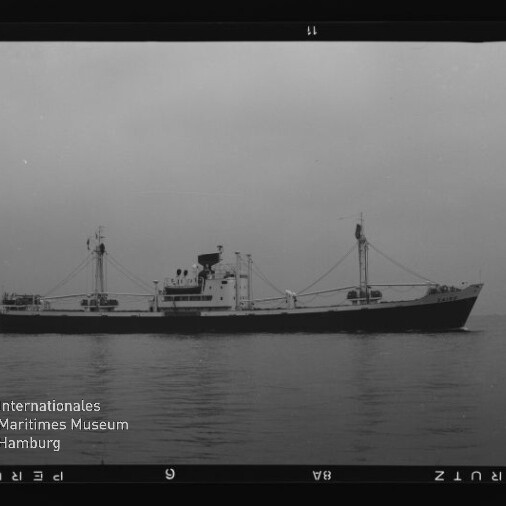 Schwarzweißfoto eines Frachters mit zwei Ladebäumen auf ruhiger See, Museumssignet Internationales Maritimes Museum Hamburg links unten.