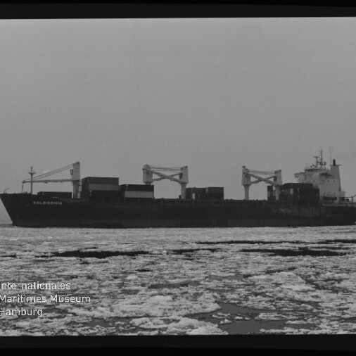 Frachtschiff mit Bordkränen und Containern fährt durch eisbedeckte See, Museum-Logo unten links.