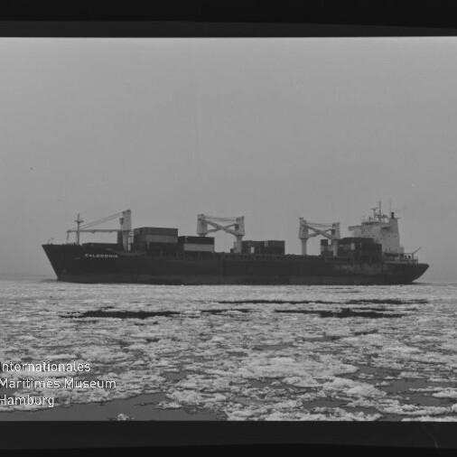 Frachtschiff mit Ladekränen fährt auf ruhiger, teilweise zugefrorener See, Vordergrund mit Treibeis und Museumslogo
