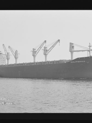 Großes Frachtschiff CALIFORNIA mit Ladekränen und einem Schlepper an ruhiger See, Schwarzweißaufnahme