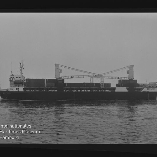 Schwarzweiß-Foto eines Frachtschiffs mit zwei Kranauslegern und Containern auf ruhiger See, Museumslogo unten links.