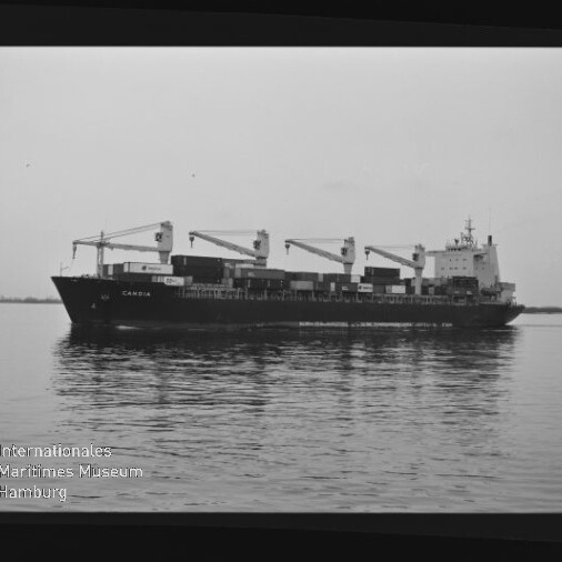 Frachtschiff mit vier Ladekränen und Containern fährt über spiegelndes Wasser; schwarz-weiß-Aufnahme.