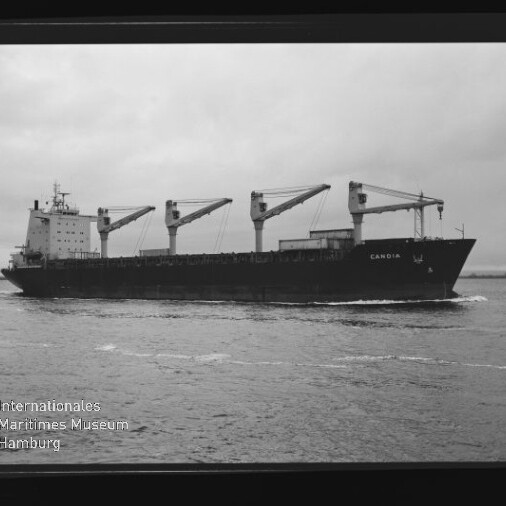 Schwarzweiß-Foto eines Frachtschiffs mit vier Ladekranen, Name CANDIR sichtbar, auf ruhigem Meer mit Museumswasserzeichen.
