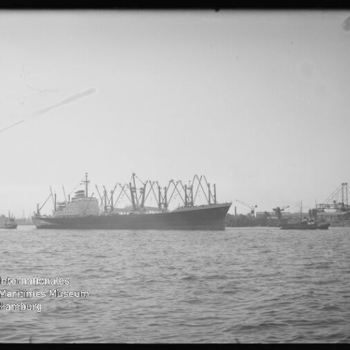 Frachtschiff mit mehreren Ladekränen im Hafen, Wasser im Vordergrund; Wasserzeichen: Internationales Maritimes Museum Hamburg