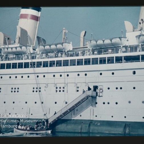Passagierschiff mit Gangway und Rettungsbooten, kleine Barkasse am Wasser und Logo des Maritimen Museums Hamburg.