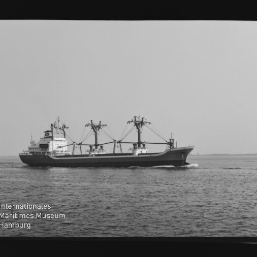 Frachtschiff mit drei Ladekränen fährt seitlich auf ruhiger See, schwarzweißes Foto mit Wasserzeichen des Maritimen Museums.