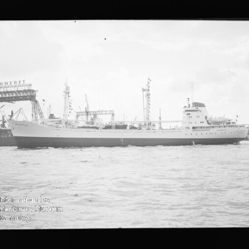 Frachtschiff im Hafen vor Werftkränen, Wasser im Vordergrund und Museumslogo unten links.