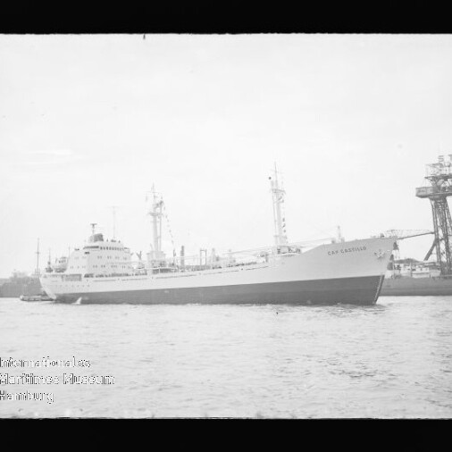 Großes Frachtschiff fährt auf ruhigem Wasser vor einem Industriehafen mit hohem Werftkran.