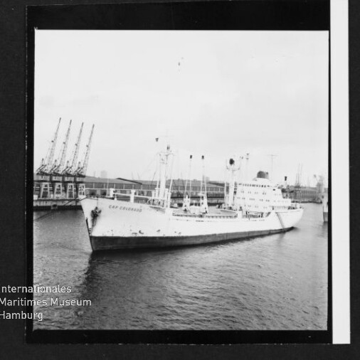 Weißes Frachtschiff im Hafen vor Krananlagen, mit Wasserzeichen des Internationalen Maritimen Museums Hamburg.