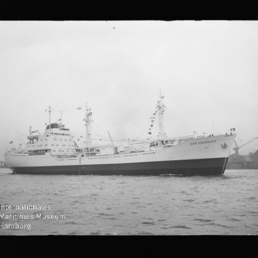 Passagier-/Frachtschiff Cap Colombie mit Masten und Ladebaum auf ruhigem Wasser, Schwarzweißaufnahme mit Museumswasserzeichen