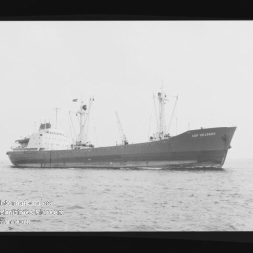 Frachtschiff Cap Delgado in Seitenansicht auf ruhiger See, mit Ladekränen und sichtbarem Schornstein.
