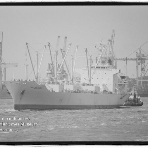 Großes Frachtschiff mit Ladekränen und Schlepper im Hafen, links Wasserzeichen Internationales Maritimes Museum Hamburg