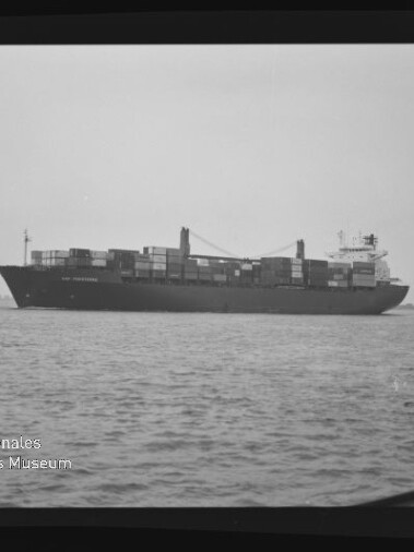 Containerschiff mit aufgestapelten Containern und Bordkränen fährt auf ruhiger See, schwarzweißes Foto.