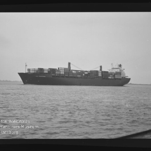 Containerschiff mit aufgestapelten Containern und Bordkränen fährt auf ruhiger See, schwarzweißes Foto.