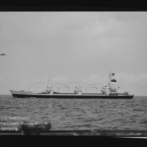 Schwarzweißaufnahme eines Frachtschiffs mit Ladekränen auf ruhiger See; unten links Stempel Internationales Maritimes Museum Hamburg.